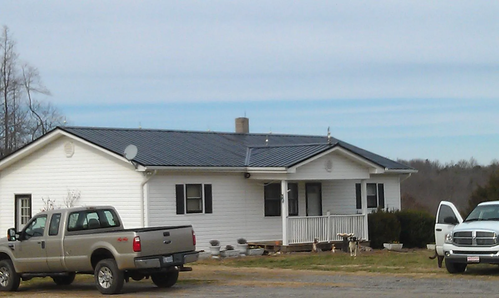 Finished dark metal roof on a white ranch home with work trucks parked in Jamestown